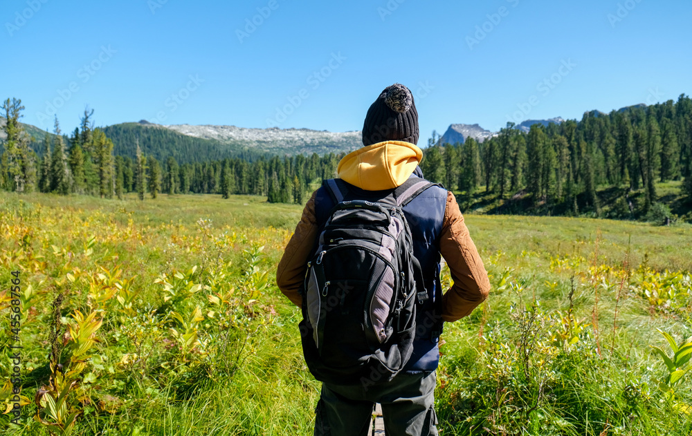 Traveller man with backpack looking to mountains. Back view.