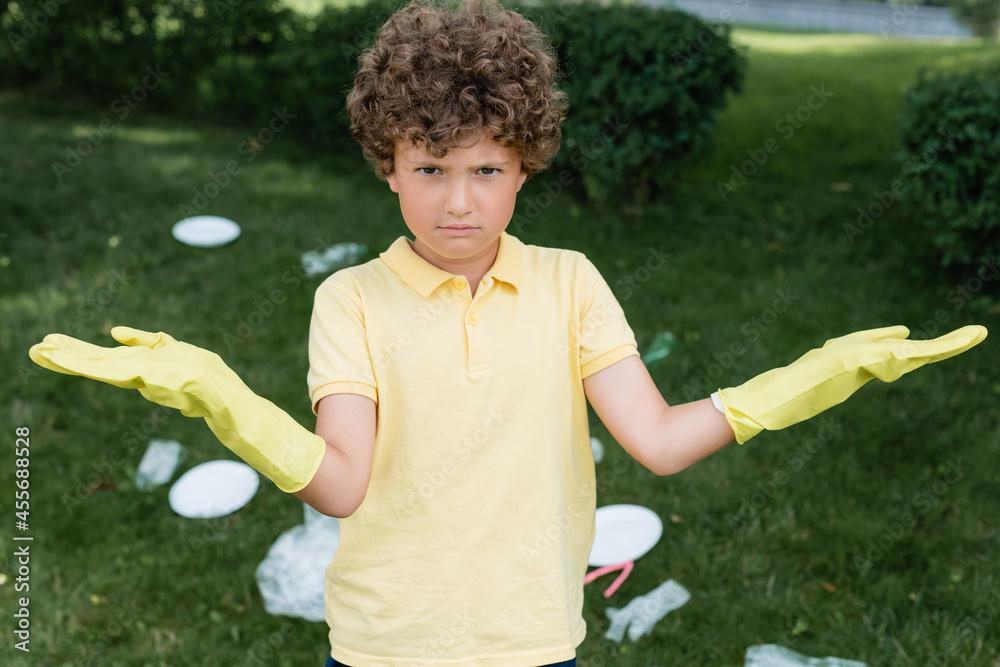Confused boy in rubber gloves looking at camera near blurred garbage outdoors Confused boy in rubber gloves looking at camera near blurred garbage outdoors