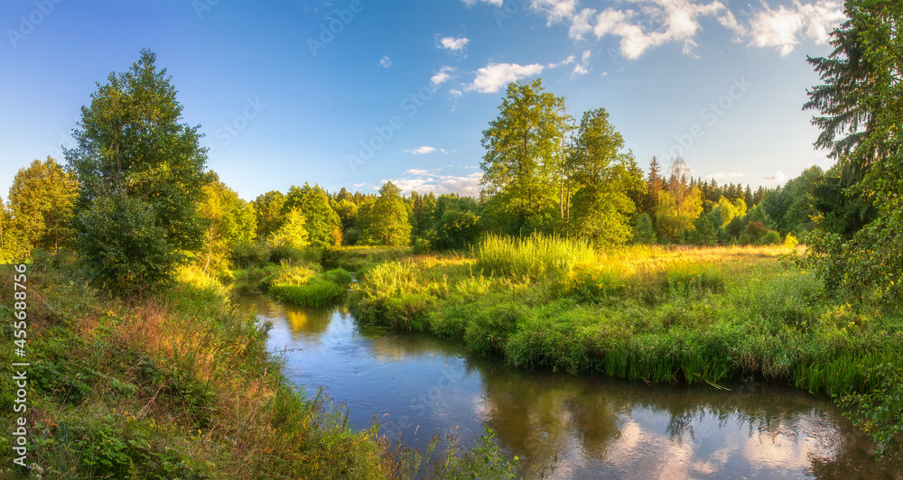 The first month of autumn. Landscape of autumn of nature. Sunset above river in the forest. Yellow grass and green bushes near river.
