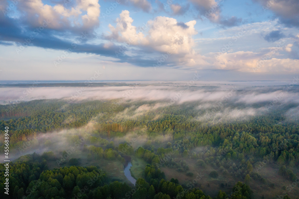 Aerial view of scenery by misty woodland. Earler morning the first day of autumn. Cloudy sunrise above misty forest.