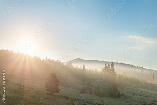 Scenic beautiful panoramic landscape view of old small wooden hut cabin on green mountain hill forest woods meadow at early morning fog misty sunrise sky time. Alpine nature travel destination