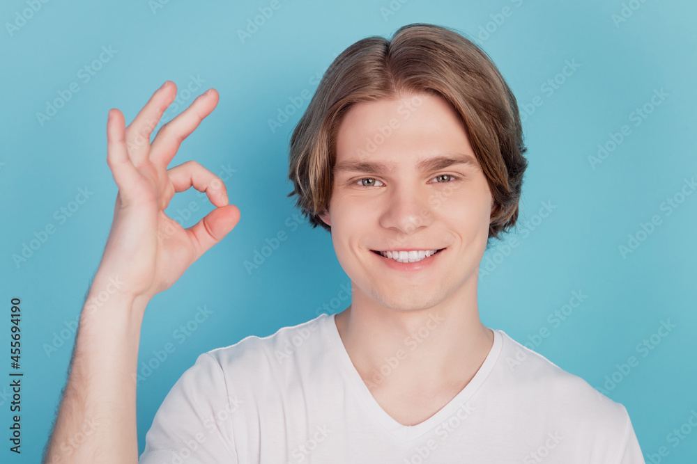Photo of positive cheerful young man show okay signs isolated on blue background