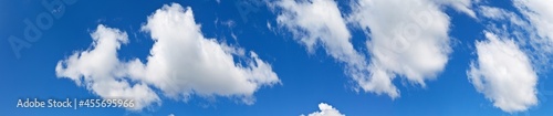 Panoramic view of the blue sky with cumulus clouds on a sunny clear day. White fluffy light clouds float across the blue sky. Heavenly bright landscape. Natural background  banner