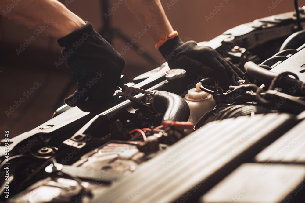 Auto mechanic repairs car. The employee carries out maintenance of the machine and shines a lamp under the hood. Operation of a mechanic under the hood of a car