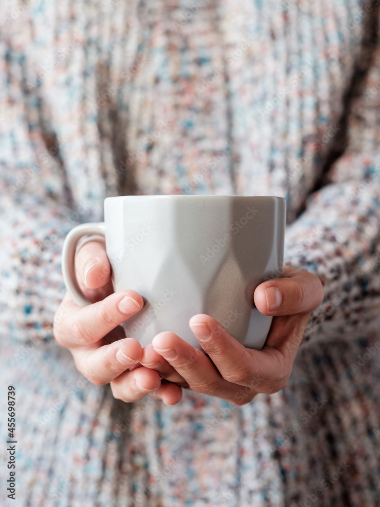 A woman dressed in a wool sweater on a cold day and holding a cup of warm tea in her hands. A woman dressed in a wool sweater on a cold day and holding a cup of warm tea in her hands.