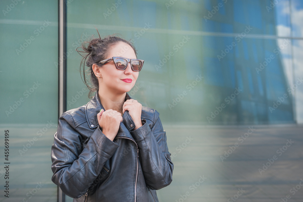 Beautiful smiling woman with sunglasses near the mirror wall of city building Beautiful smiling woman with sunglasses near the mirror wall of city building