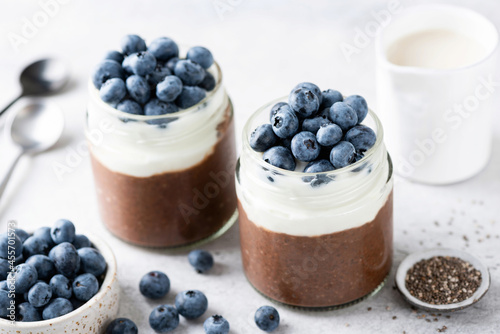 Chocolate chia pudding with yogurt layer and blueberries in a jar, closeup view. Healthy dessert or sweet snack