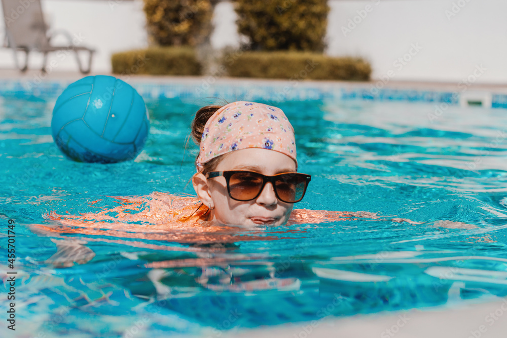 Preteen girl wearing sunglasses swimming in pool with blue water. Healthy and safe summer outdoor activities.