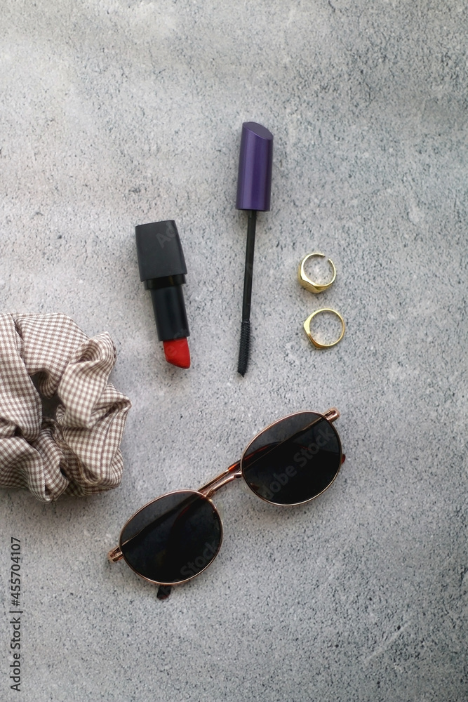 Retro sunglasses, scrunchie, gold rings, red lipstick and mascara on concrete background. Flat lay. Retro sunglasses, scrunchie, gold rings, red lipstick and mascara on concrete background. Flat lay.
