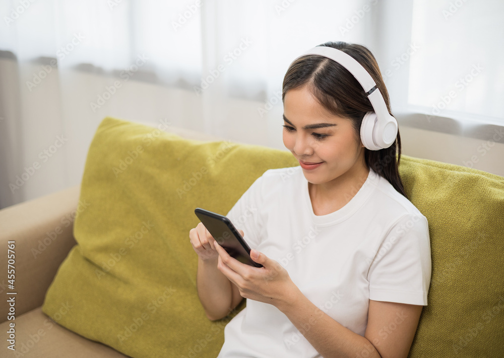 Relaxing time on sofa. Beautiful young asian woman sitting on sofa she choose music from smartphone take a rest and listening song with headphone. Lifestyle in living room at house in the morning. Relaxing time on sofa. Beautiful young asian woman sitting on sofa she choose music from smartphone take a rest and listening song with headphone. Lifestyle in living room at house in the morning.