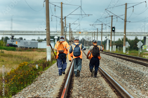 workers in orange uniforms walk along the railway tracks. the repair team is going to work by rail. stone embankment of the railway and power lines. it is dangerous to walk on railway tracks photo