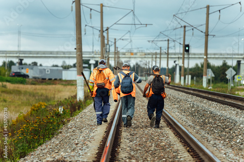 workers in orange uniforms walk along the railway tracks. the repair team is going to work by rail. stone embankment of the railway and power lines. it is dangerous to walk on railway tracks