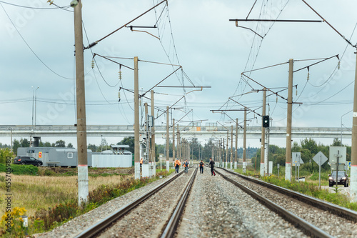 workers in orange uniforms walk along the railway tracks. the repair team is going to work by rail. stone embankment of the railway and power lines. it is dangerous to walk on railway tracks