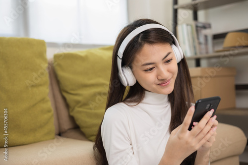 Relaxing time in living room. Beautiful young asian woman choose music from smartphone take a rest and listening song with headphone and dancing. Lifestyle in living room at house in the morning.