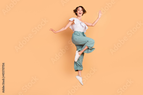 Photo of adorable funny young woman dressed striped top jumping high isolated beige color background