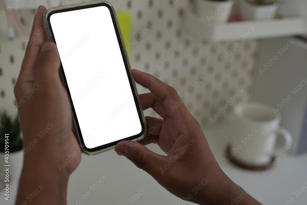 Cropped image of hands using a white blank screen smartphone over the modern desk as background. Cropped image of hands using a white blank screen smartphone over the modern desk as background.