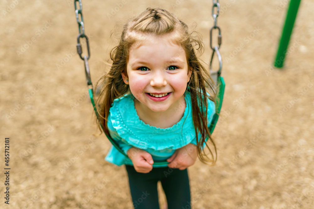 Happy little girl is playground having fun on swing