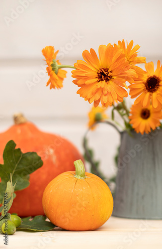 Bright orange pumpkins and marigold flowers on a light wooden background, autumn still life, vertical image.