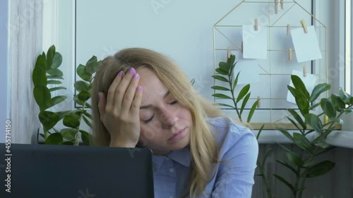 Tired sleepy young caucasian woman worker at desk workplace. Overworking and sleeping deprivation. Businesswoman and Monetary crisis. Freelancer in depression. Sad Woman looking at a laptop at workspa photo