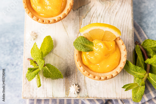 Bilde på lerret Shortbread tartlet filled with lemon curd, mint and lemon slices and mini meringue on wooden board, blue concrete background