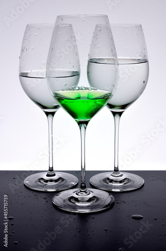 Three wineglasses two with water one with a green magic potion absinthe