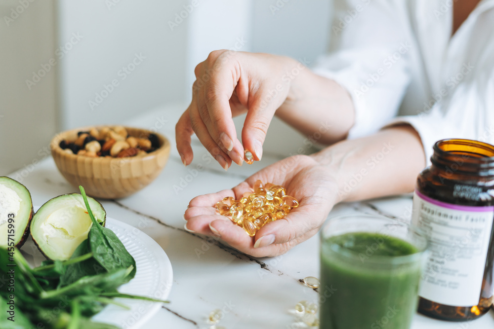 Woman doctor nutritionist hands in white shirt with omega 3, vitamin D capsules with green vegan food. The doctor prescribes a prescription for medicines and vitamins at clinic - obrazy, fototapety, plakaty 
