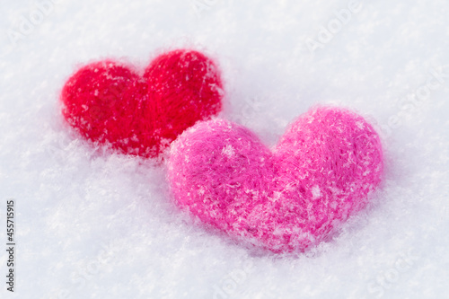 Two woolen toy hearts lying on the white snow in winter morning. Valentines day concept.