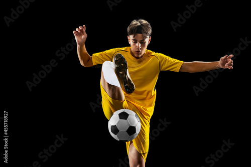 Full-length bacl view portrait of young man, football player training isolated on black background. Dribbling photo