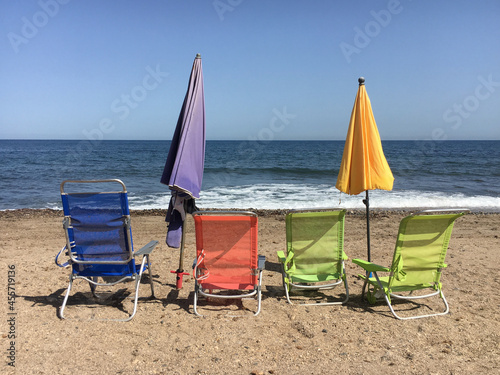 Four beach loungers facing the sea on the beach, with two closed umbrellas