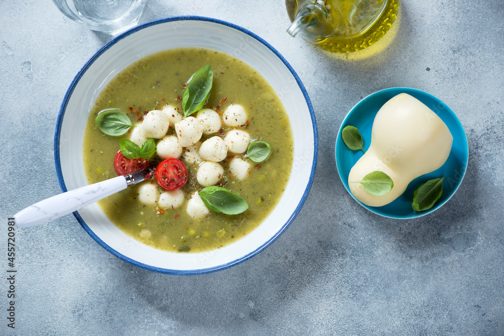 Vegetable soup with green peas, spinach, leek and scamorza cheese, flatlay on a light-blue stone background, horizontal shot Vegetable soup with green peas, spinach, leek and scamorza cheese, flatlay on a light-blue stone background, horizontal shot