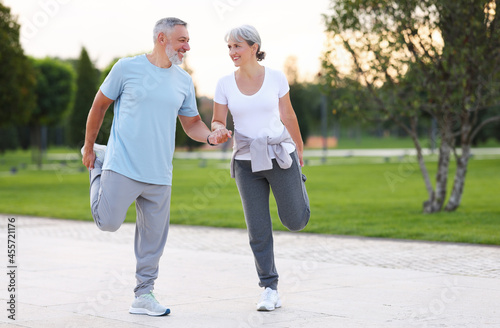 Smiling senior man and woman doing legs stretching exercises helping each other by holding hands