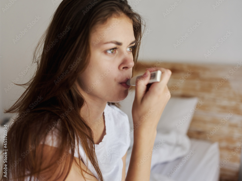 woman sitting on bed in hotel mouth thermometer checking temperature woman sitting on bed in hotel mouth thermometer checking temperature