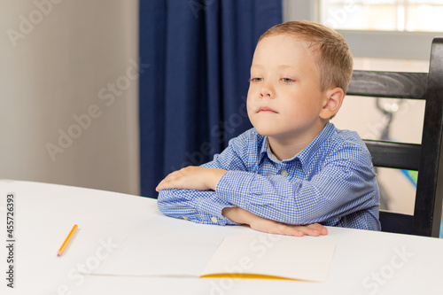 Cute seven year old child boy doing homework at home on a white wooden table during a pandemic. Selective focus. Close-up. Portrait