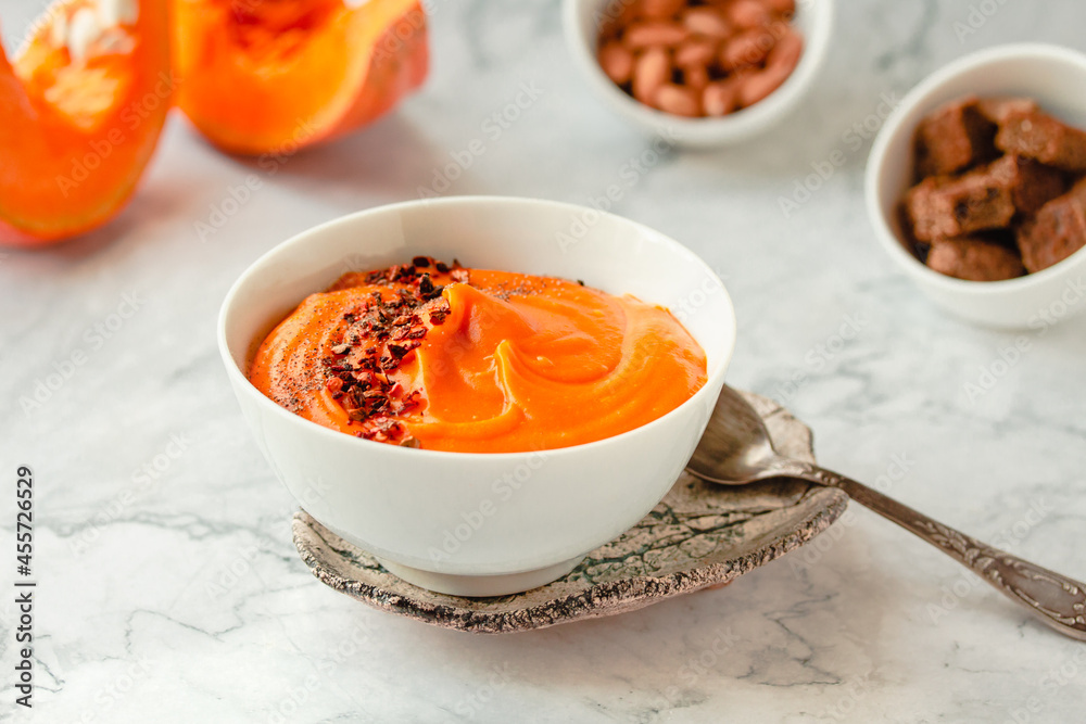 Pumpkin soup and organic pumpkins on marble table. Seasonal autumn food - Spicy pumpkin and carrot soup Pumpkin soup and organic pumpkins on marble table. Seasonal autumn food - Spicy pumpkin and carrot soup