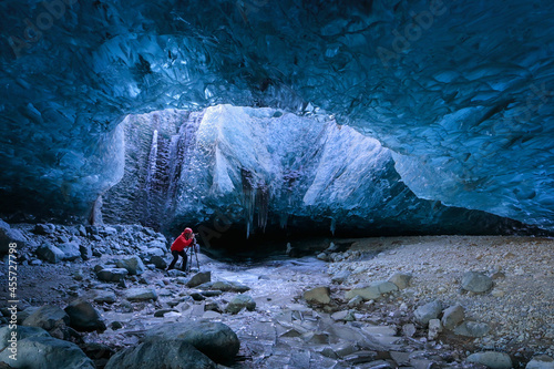 Photographer standing underground inside of a glacier, climate specific, vatnajokull National Park, amazing nature of Skaftafell, Entrance of an ice cave,Iceland photo