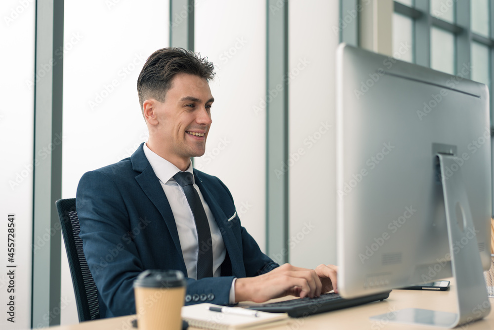 Adult smart business man in suit outfit sitting and working in front of computer typing keyboard in modern office Adult smart business man in suit outfit sitting and working in front of computer typing keyboard in modern office