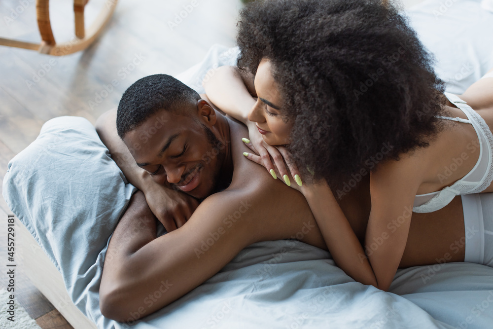 Obraz premium High angle view of african american woman in bra lying on smiling boyfriend in bedroom.