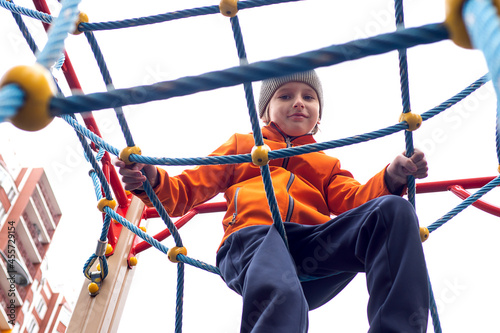 Funny caucasian blond boy in an orange jacket plays on the sports playground. © Svetlana Glazkova