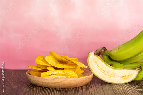 Banana chip or locally known as kerepek pisang in wooden plate with raw halved banana and banana bunch. Selective focus points. Blurred background photo