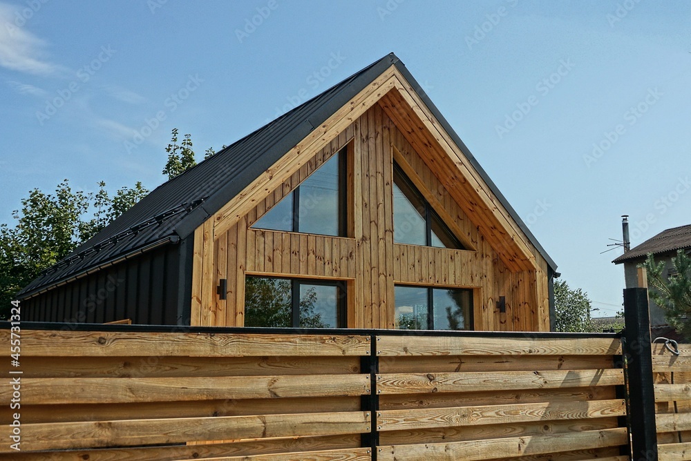 private brown wooden house with large windows behind a wall of fence made of planks on the street