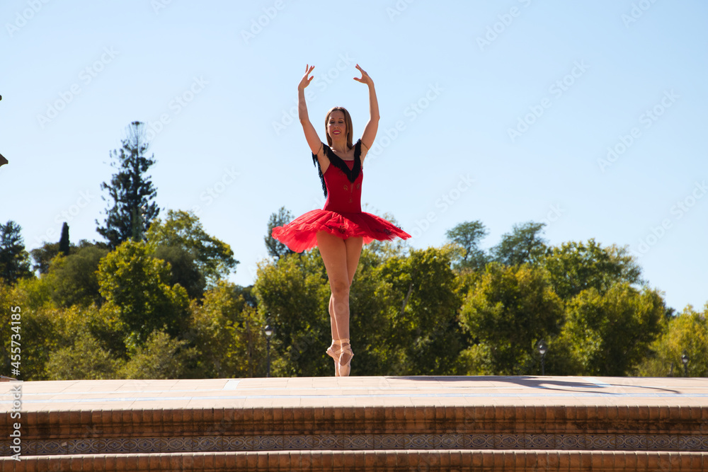 ballet dancer in red tutu dancing in the street. The ballerina is doing different ballet postures and movements. Classical ballet concept.