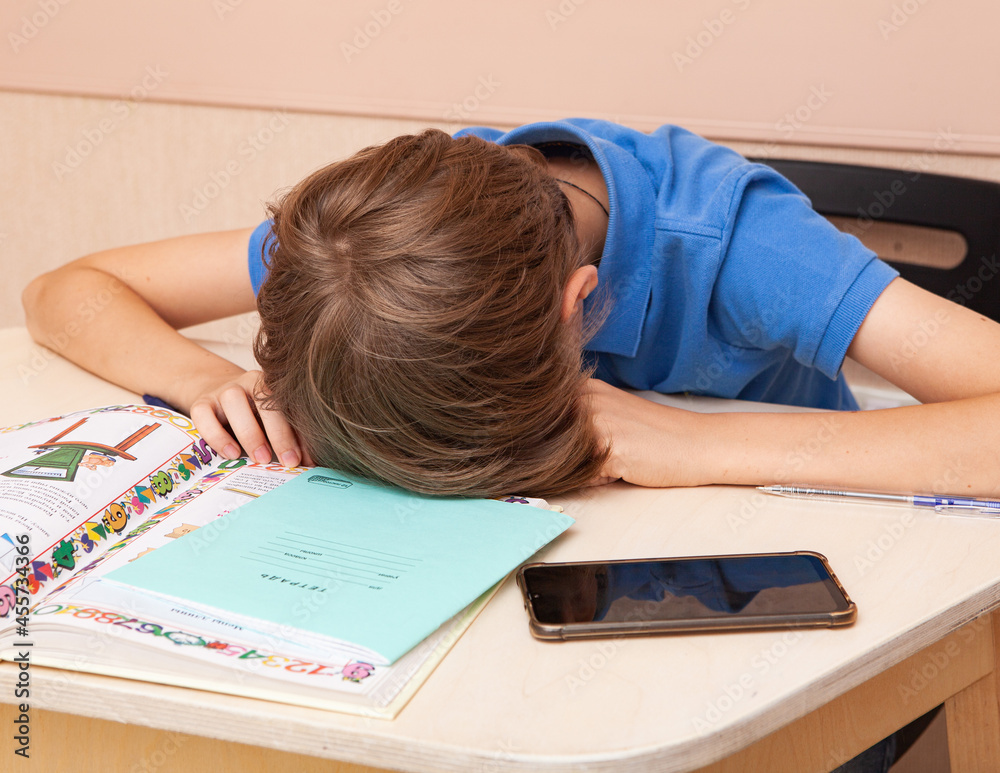Naklejka premium The boy is tired of doing homework. He lowered his head to the table.