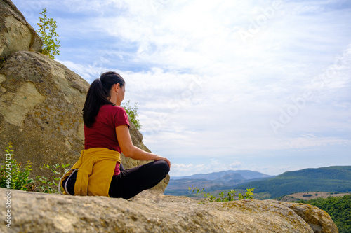 Happy woman sitting on a rock on top of mountain. Female doing yoga and meditating in the nature. wearing casual attire