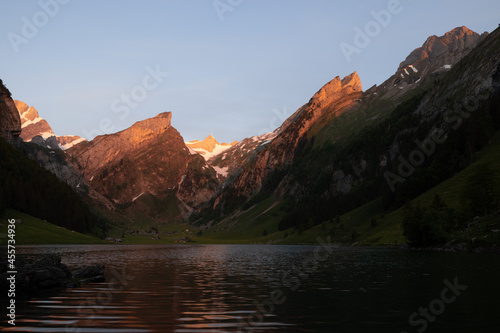 Epic sunrise by an alpine lake in Switzerland called Seealpsee. The sun shines to the peak of the mountain on the other side of the lake. This looks so wonderful.