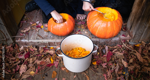 Little girls make jack-o-lantern from big pumpkins for celebratiion of halloween holiday.Witch costume, hat, coat. Cut with knife,take out pulp with seeds.Outdoors activity, backyard.Children's party photo