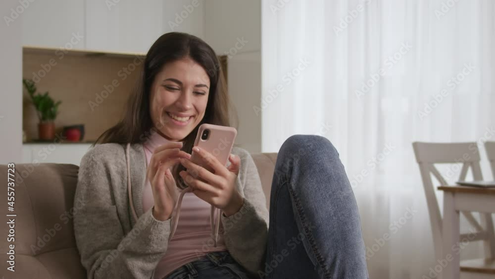 Young caucasian woman laughs at what she sees on her smart phone while browsing the social media on the web Young caucasian woman laughs at what she sees on her smart phone while browsing the social media on the web