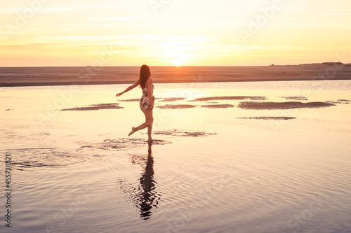 Elegant woman in short dress running on water on the beach during sunset photo