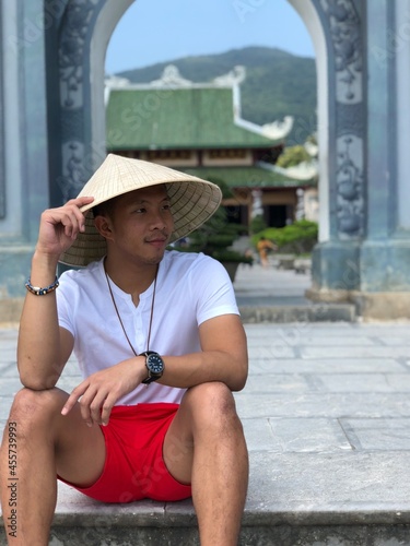 Man with conical hat sitting outdoor near a temple photo