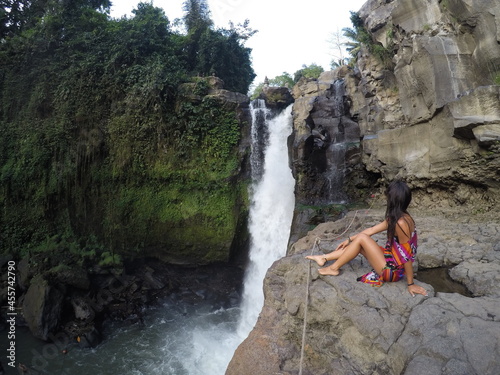 Woman sitting on rock and looking at waterfall nearby