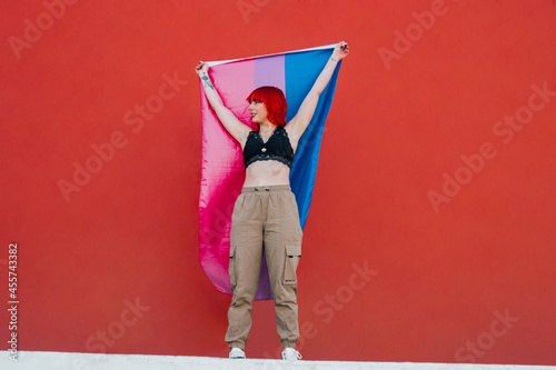 Young woman waving bisexual pride flag standing against red background photo